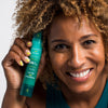 Woman holding bottle of Urban Skin RX YouthHero AM/PM Serum next to her face