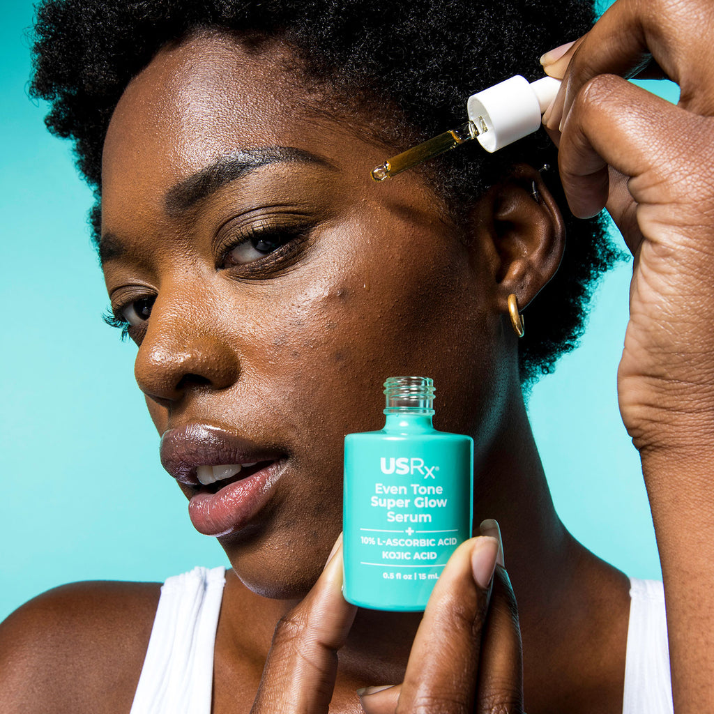 Woman applying Urban Skin Rx skincare Even Tone Super Glow Serum to her face with a dropper against a teal background